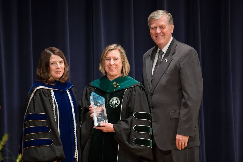 A faculty member is holding her award for a picture with President Emeritus Haas and the Provost.